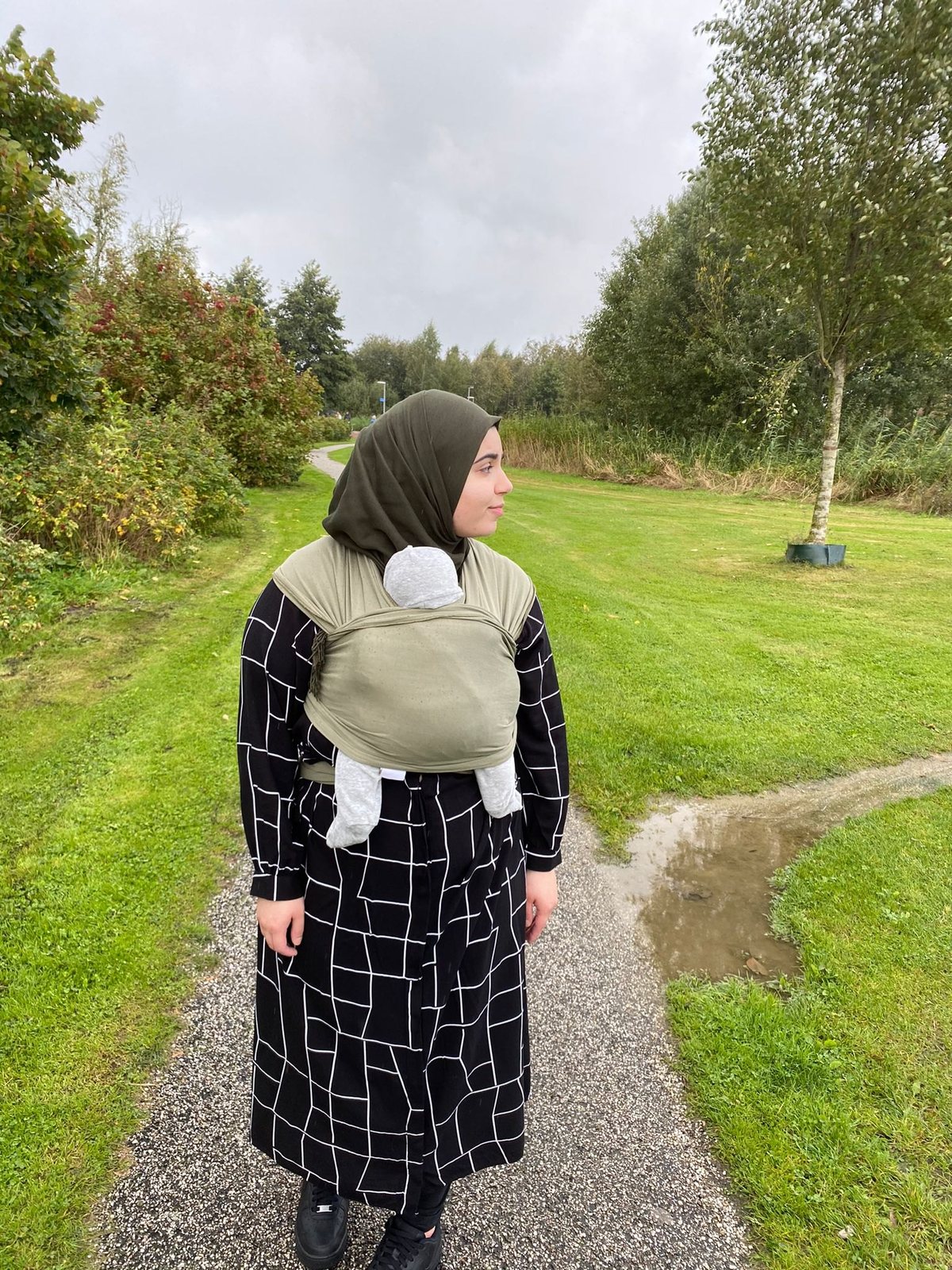 Van achteren gezien: een kind op de rug in een groene draagzak