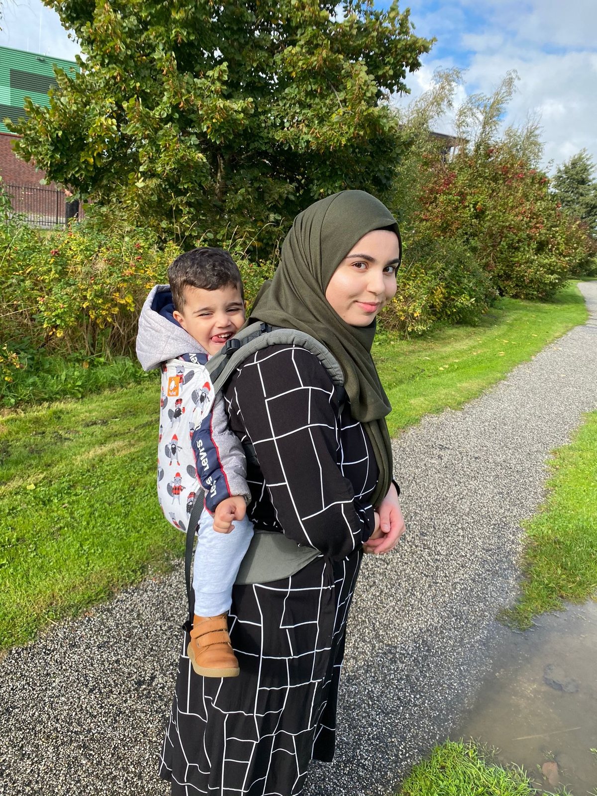 Een lachende peuter op de rug in een draagzak, op een wandelpad